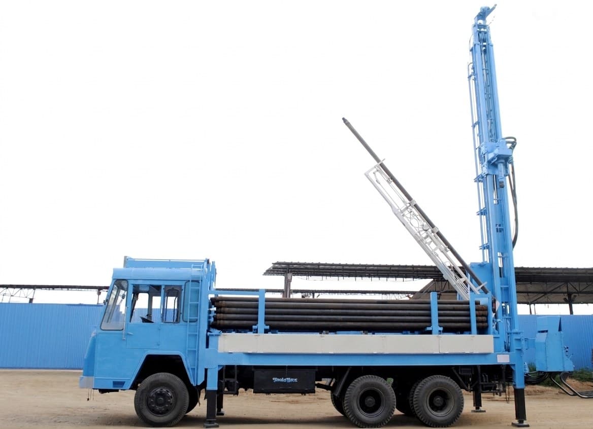 Velson Model-I truck-mounted water-well rig, mast raised at the rear with drill rods racked along the deck
